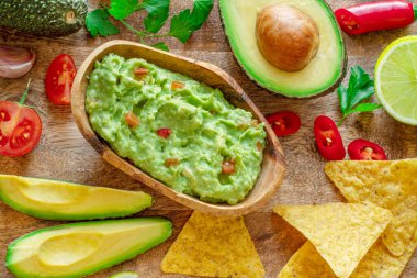 Guacamole, guacamole malzemeleri ve tahta arka planda cips. Düz yatıyordu.