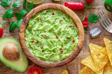 Guacamole, guacamole malzemeleri ve tahta arka planda cips. Düz yatıyordu.