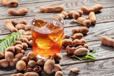 Glass of cool refreshing tamarind drink and some tamarind fruit on wooden table.