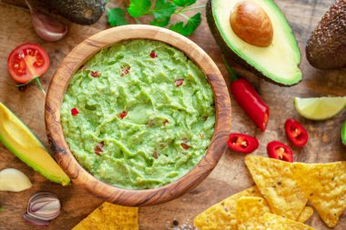 Guacamole, guacamole malzemeleri ve tahta arka planda cips. Düz yatıyordu.