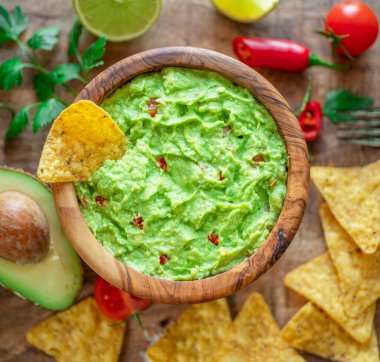 Guacamole, guacamole malzemeleri ve tahta arka planda cips. Düz yatıyordu.