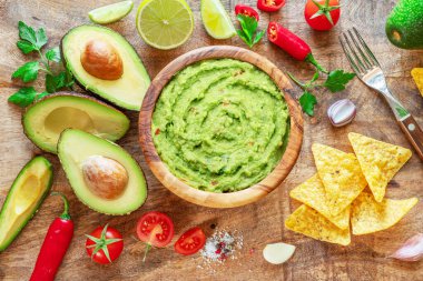 Guacamole, guacamole malzemeleri ve tahta arka planda cips. Düz yatıyordu.