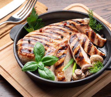 Kızarmış tavuk filetosu ve mantarla ahşap masadaki tavada otlar..