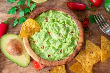 Guacamole, guacamole malzemeleri ve tahta arka planda cips. Düz yatıyordu.