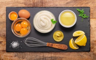 Homemade mayonnaise and mayo ingredients on black stone slate serving plate. Flat lay.