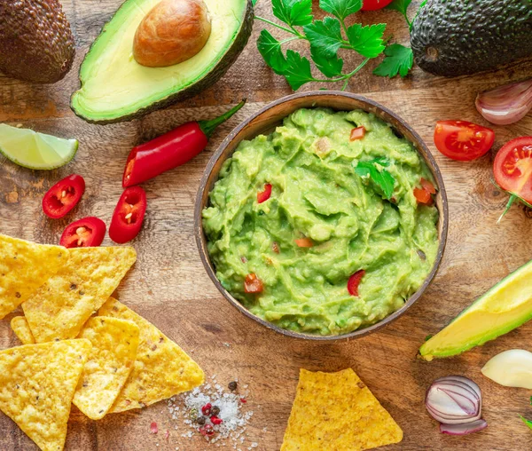 Guacamole, guacamole malzemeleri ve tahta arka planda cips. Düz yatıyordu.