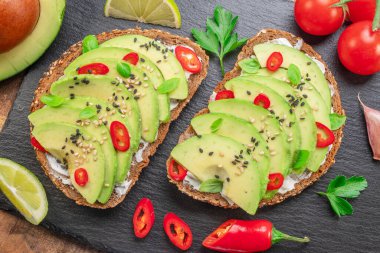 Avokado tostları - avokado dilimli ekmek, kırmızı biber parçaları ve siyah taş tahtada susam..