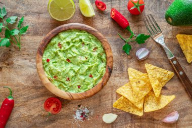 Guacamole, guacamole malzemeleri ve tahta arka planda cips. Düz yatıyordu.
