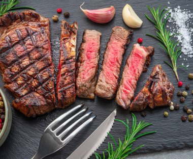 Grilled  delicious ribeye steak slices and some seasonings on black slate serving plate. Flat lay.