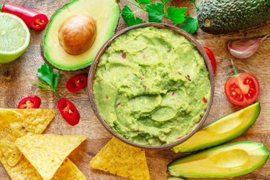 Guacamole, guacamole malzemeleri ve tahta arka planda cips. Düz yatıyordu.