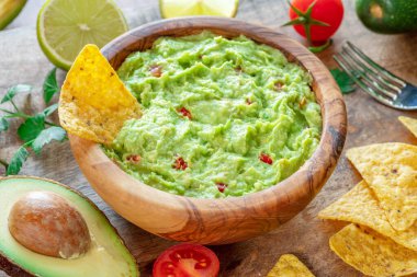 Guacamole, guacamole ingredients and chips on wooden background.  clipart