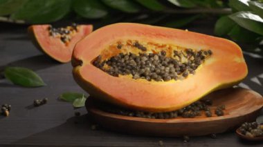 Yarım papaya meyvesi ve tropikal bitki yapraklarıyla birlikte antika bir masa üzerinde tohum. Tahta kaşıkla bir el tohumlardan papaya meyvesini temizler. Kameranın soldan sağa yatay yavaş hareketi. 