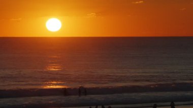Büyük Güneş 'le Portekiz' in Atlantik Okyanusu 'nda güzel bir akşam gün batımı. Dalgalarda sörfçüler. 
