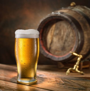 Bir bardak soğuk bira ve arka planda ahşap bira fıçısı.. 