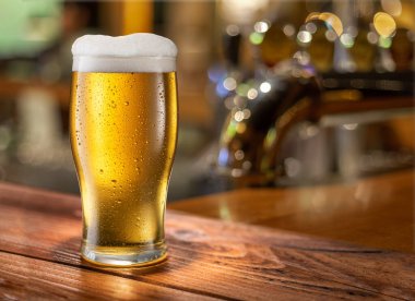Bir bardak soğuk bira ahşap bar masasının üstünde ve arka planda bulanık barın iç tarafında..