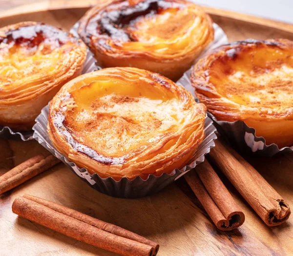 Pastel de nata turtaları ve tarçın çubukları ahşap tepside. 