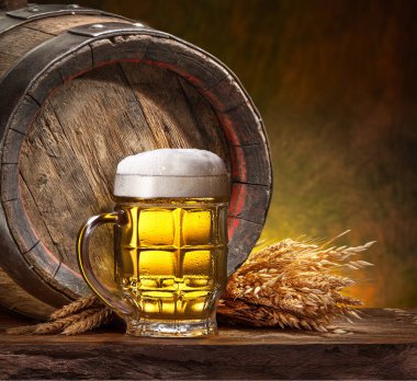 Bir kupa soğuk bira, buğday kulakları ve ahşap masada ahşap bira fıçısı..