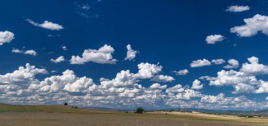 Kırsal alan, tepeler ve kümülüs bulutlarıyla çarpıcı bir gökyüzü..