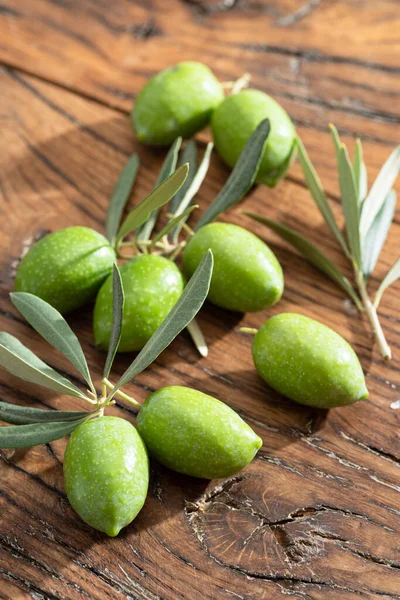 Green natural olives with olive leaves on a vintage old wooden table.