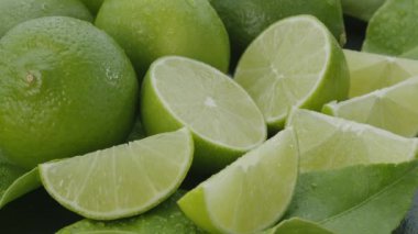 Olgun kireç meyveleri dilimler ve limon yapraklarıyla gri bir taş masanın üzerinde yavaşça hareket eder. Projelerin için güzel bir meyve arka planı. Makro video çekimi.