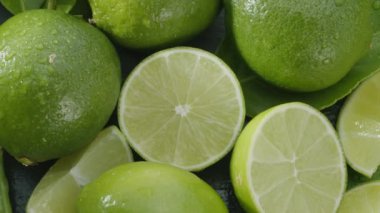 Olgun kireç meyveleri dilimler ve limon yapraklarıyla gri bir taş masanın üzerinde yavaşça hareket eder. Projelerin için güzel bir meyve arka planı. Makro video çekimi.