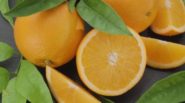 Olgun portakal meyveleri dilimler ve portakal ağacı yapraklarıyla gri bir taş masanın üzerinde yavaşça hareket eder. Projelerin için güzel bir meyve arka planı. Makro video çekimi.