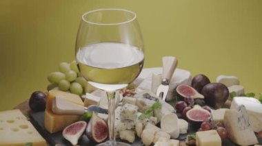 Bir bardak beyaz şarap, çeşitli dilimlenmiş peynirli meyve, nane, fındık ve peynir bıçakları çerçevede yavaşça döner. Projeleriniz için harika peynir ve şarap arka planı..