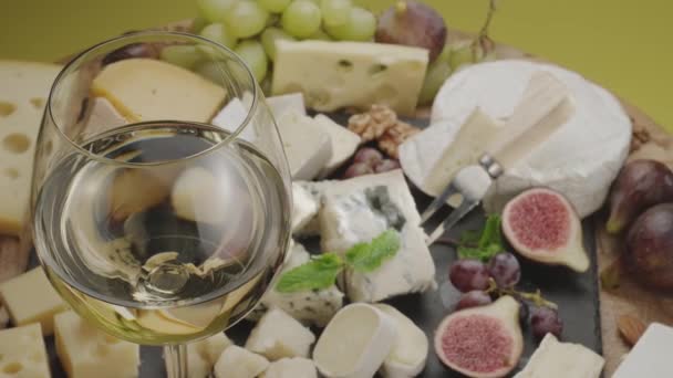 フルーツ ミント ナッツ チーズ切断ナイフの様々なスライスチーズがフレームでゆっくりと回転する白ワインのグラス あなたのプロジェクトのための素晴らしいチーズとワインの背景 — ストック動画