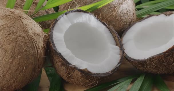 ココナッツ スライス ココナッツの葉とともに新鮮なオープンココナッツが木製のテーブルにゆっくりと回転しています あなたのプロジェクトのための素晴らしいフルーツの背景 — ストック動画