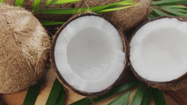 ココナッツ スライス ココナッツの葉とともに新鮮なオープンココナッツが木のテーブルでゆっくり回転しています — ストック動画