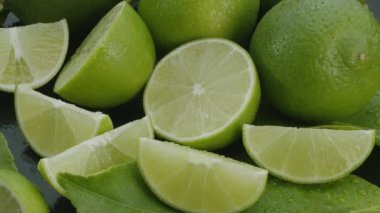 Olgun kireç meyveleri dilimler ve limon yapraklarıyla gri bir taş masanın üzerinde yavaşça hareket eder. Projelerin için güzel bir meyve arka planı. Makro video çekimi.