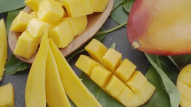 Olgun mango meyveleri, dilimler ve mango yapraklarıyla gri taş bir masanın üzerinde yavaşça hareket eder. Projelerin için güzel bir meyve arka planı. Makro video çekimi.