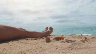Güneşli bir yaz gününde kumlu bir sahilde oturan bir kadın. Ön planda güzel dişi bacakları yavaşça hareket ediyor. Sinema stili.