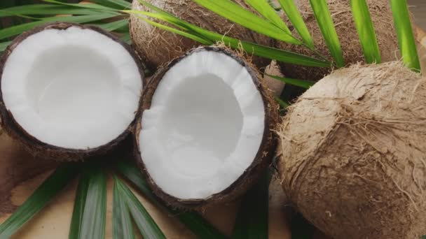 ココナッツ スライス ココナッツの葉とともに新鮮なオープンココナッツが木製のテーブルにゆっくりと回転しています あなたのプロジェクトのための素晴らしいフルーツの背景 — ストック動画