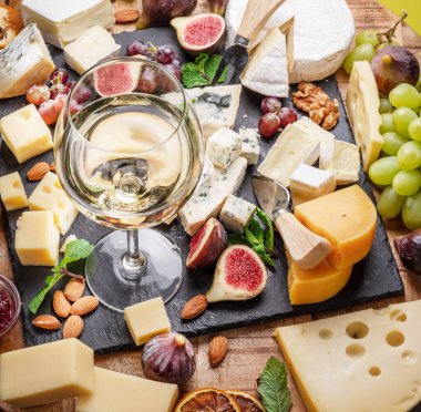 Bir bardak beyaz şarap, çeşitli dilimlenmiş peynirli meyve, nane, fındık ve peynir bıçakları. Projeleriniz için harika şarap ve peynir arka planı..