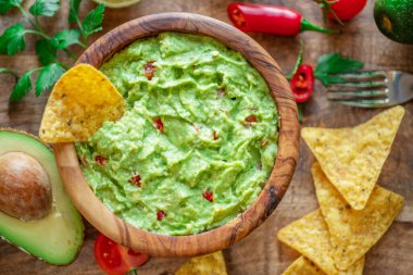 Guacamole, guacamole malzemeleri ve tahta arka planda cips. Düz yatıyordu.