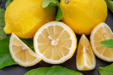 Gri taş bir masada dilimler ve limon yapraklarıyla olgun limon meyveleri. Projeleriniz için güzel meyve arkaplanı.. 