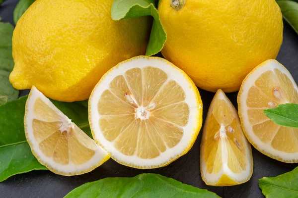 Ripe lemon fruits with slices and lemon leaves on a gray stone table. Nice fruit citrus background for your projects.
