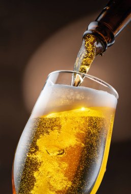 Şişeden çıkan biralar bira bardağına dökülüyor, bu da bir sürü köpüğe ve köpüğe neden oluyor. Koyu kahverengi arkaplan.