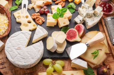 Variety of sliced cheeses with fruits, mint, nuts and cheese cutting knives. Wonderful cheese background for your projects. clipart