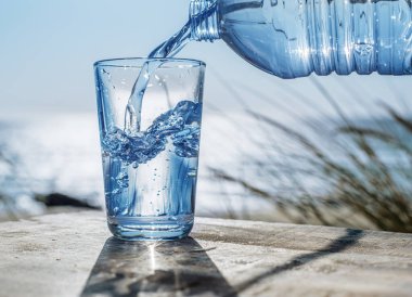Plastik şişeden bardağa su dökmek. Doğa arkaplanı.