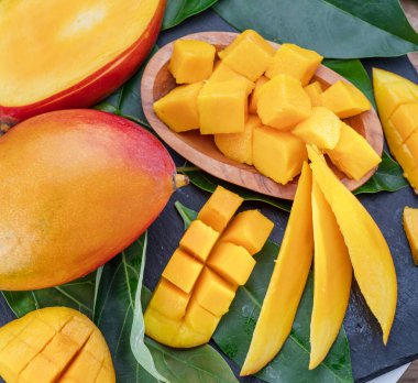 Gri bir masa üzerinde dilimler ve mango yapraklarıyla olgun mango meyveleri. Projeleriniz için güzel meyve arkaplanı.
