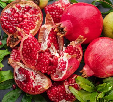 Ripe pomegranate fruits with slices and pomegranate tree leaves on a gray stone table. Nice fruit exotic background for your projects. clipart