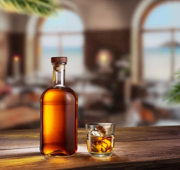Glass of whiskey and whiskey bottle on old wooden table and blurred cafe interior at the background.