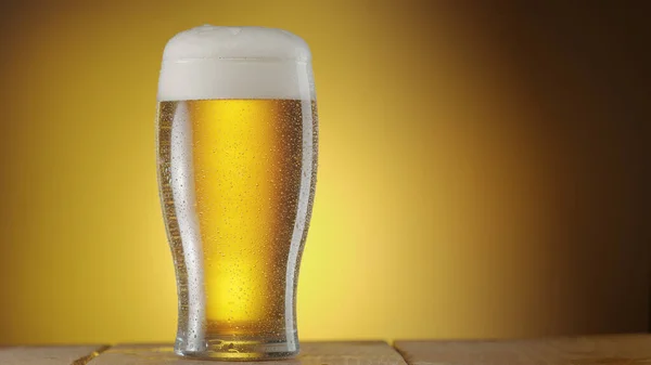 Glass of chilled beer with large head of foam isolated on yellow background.