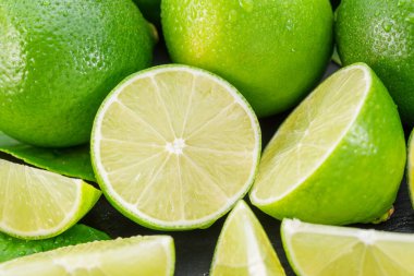 Gri taş bir masada dilimler ve limon yapraklarıyla olgun kireç meyveleri. Projeleriniz için güzel meyve arkaplanı.. 