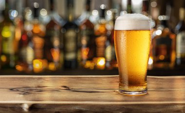 Bir bardak soğuk bira ahşap bar masasının üstünde ve arka planda bulanık barın iç tarafında..