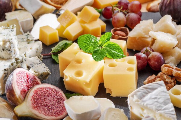 Variety of sliced cheeses with fruits, mint, nuts and cheese cutting knives. Wonderful cheese background for your projects.