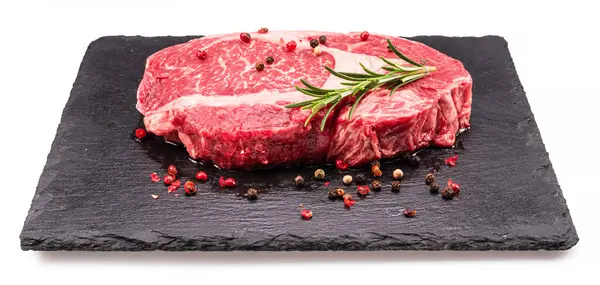 Rohe Ribeye Steak Mit Pfefferkörnern Und Rosmarin Auf Graphit Servierbrett lizenzfreie Stockbilder