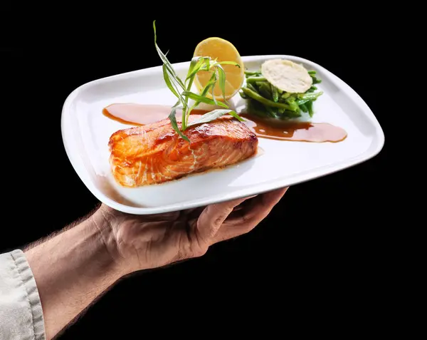 厨师拿着烤鲑鱼的白盘 旁边放着黑色背景的绿豆 味道鲜美 图库图片
